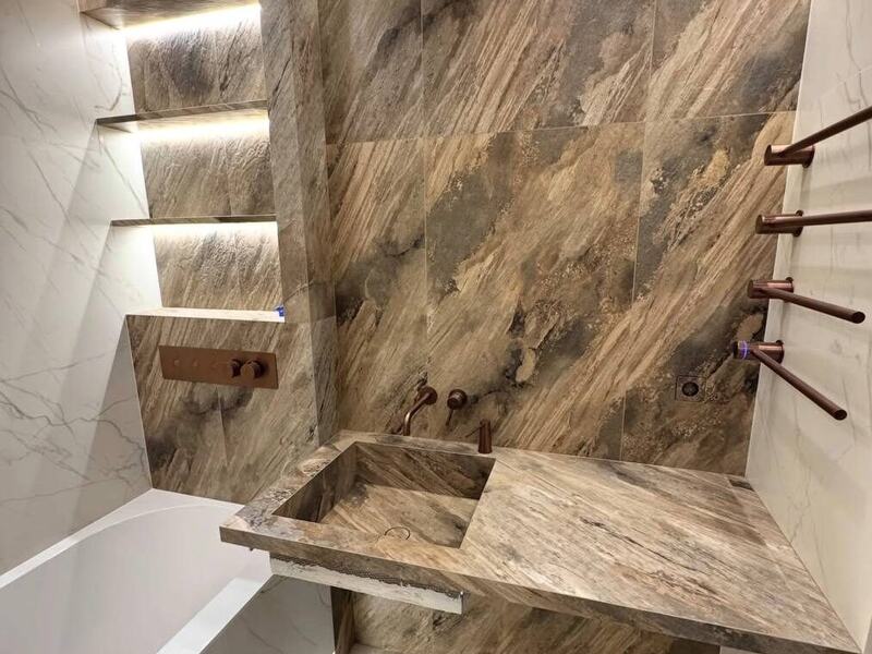 Bathroom with stone slab walls, a floating stone sink, and lit wall shelves