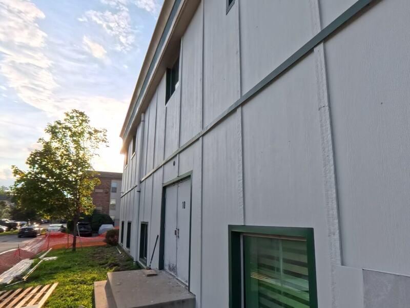 Two-story building finished in light panel siding with dark green window trim