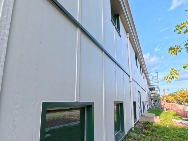Long wall of light panel siding with green-trimmed windows
