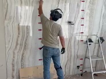 Installer setting large stone-look slabs on a feature wall with leveling clips