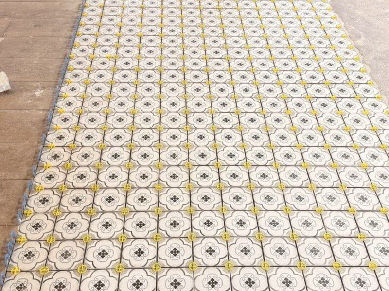 Patterned floor tile laid out with yellow leveling clips before grout